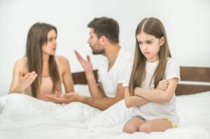 Parents fighting with daughter sitting on the bed.